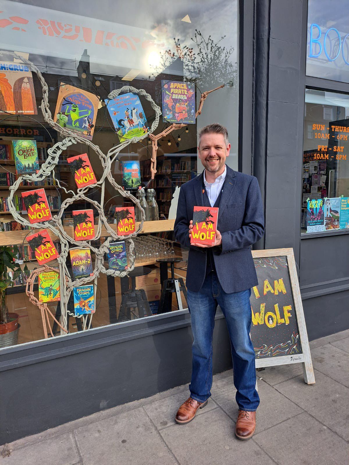 Alastair Chisholm standing in front of a shop window showing several copies of his book I Am Wolf