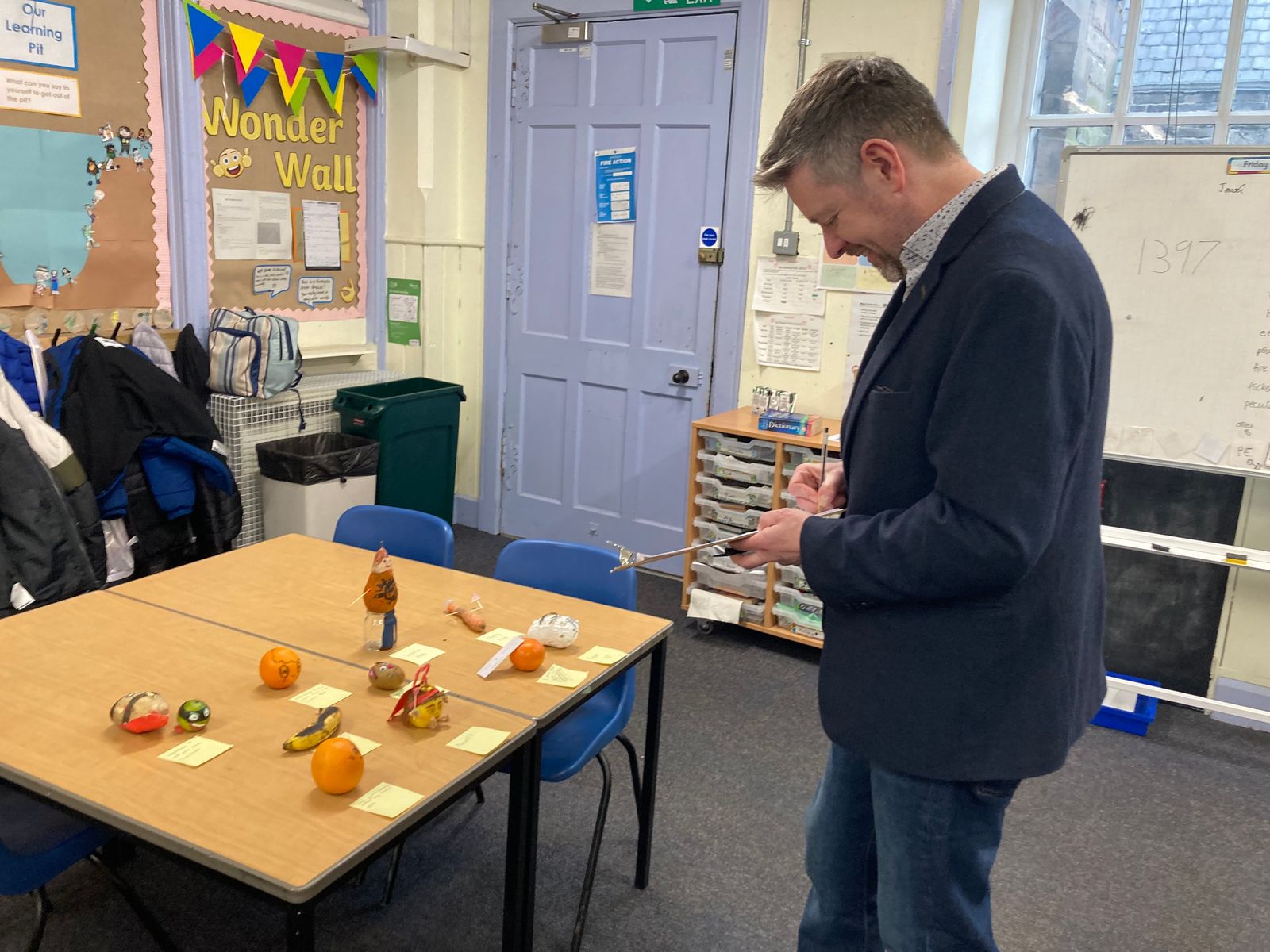 Alastair Chisholm standing before a table of fruit and veg carved and drawn to look like literary characters.