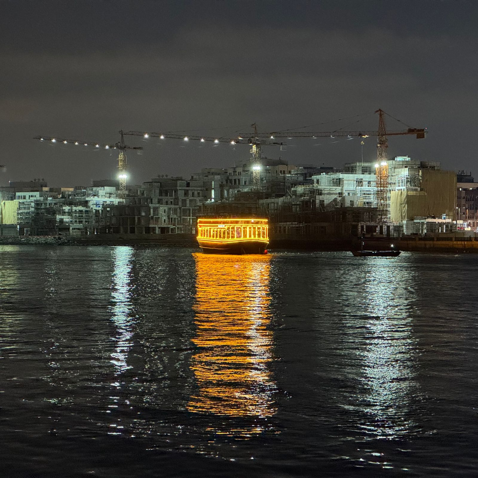 A boat on the water at night. The boat is brightly lit and its reflection shimmers on the dark water