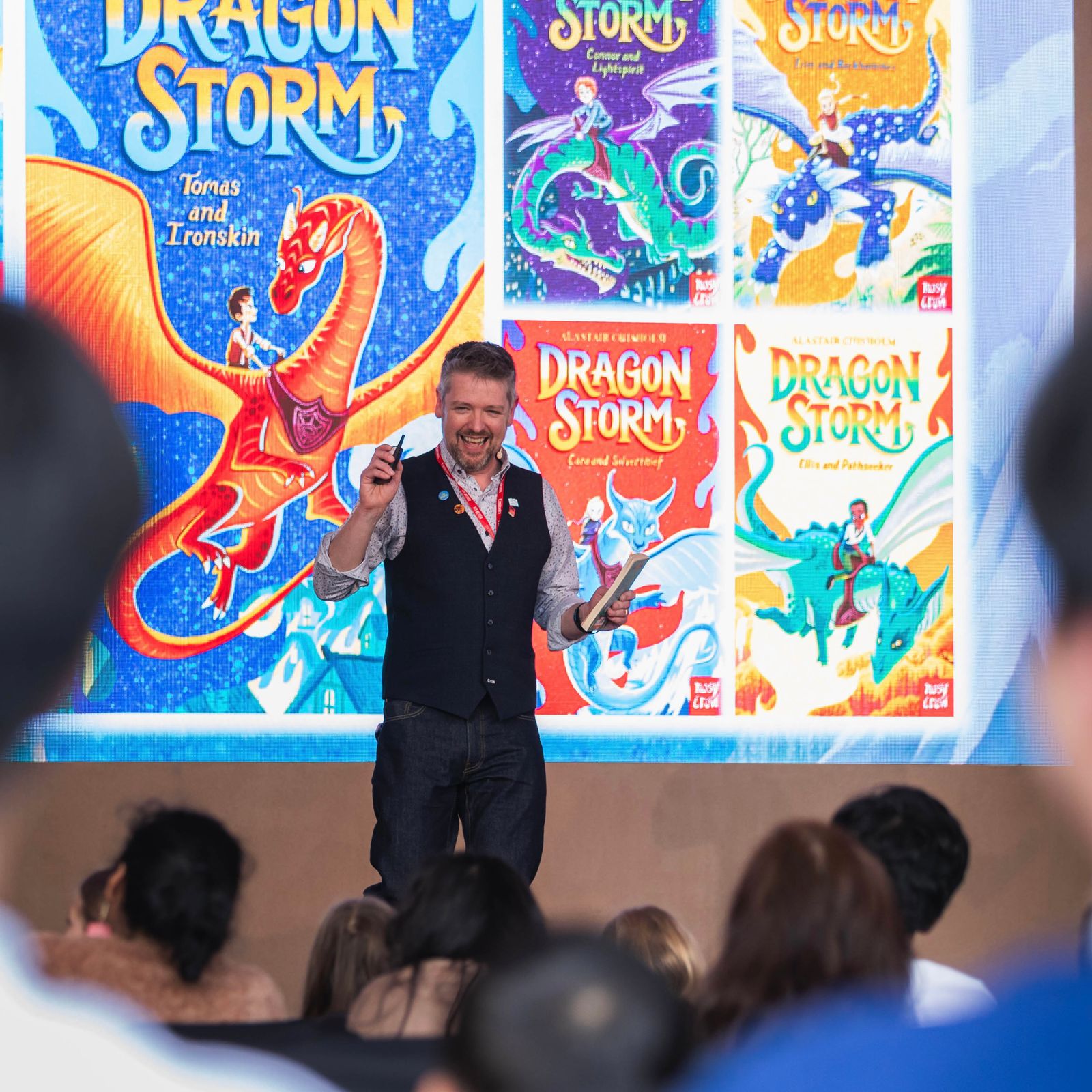 Alastair on stage in front of a large screen showing his Dragon Storm books
