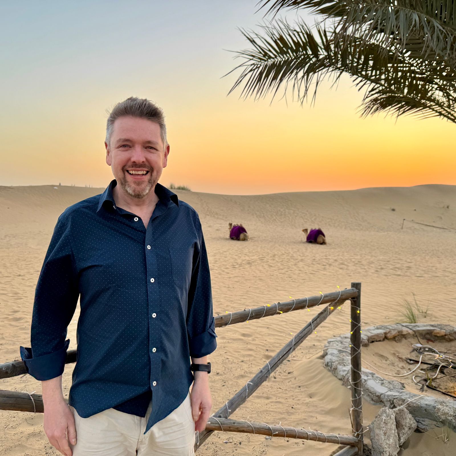 Alastair standing in the desert with camels in the background