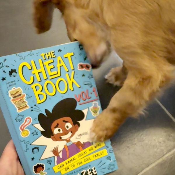 A small red dog chewing on the corner of a copy of The Cheat Book